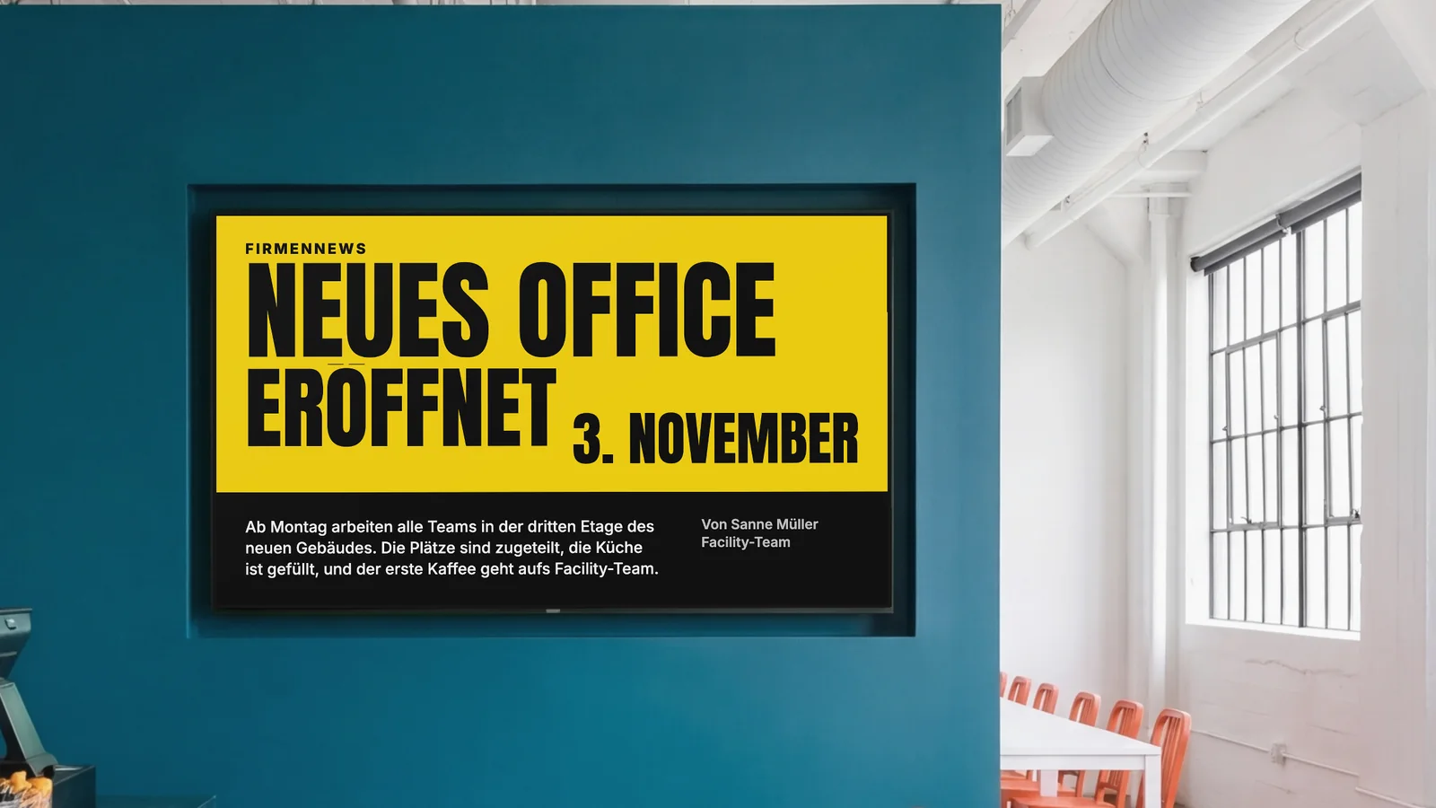 Betriebskantine mit einem Bildschirm in einer dunkelpetrolfarbenen Wand, einem Blick auf die Theke und orangefarbenen Stühlen an der Seite. Auf dem Bildschirm steht: Firmennews, neues Office eröffnet, 3. November.