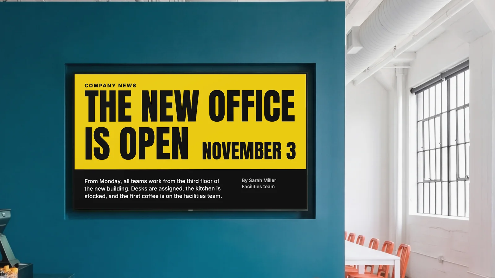 Staff canteen with a screen set into a deep teal wall, a glimpse of the counter and orange chairs at the sides. The screen reads Company News: the new office is open, November 3.