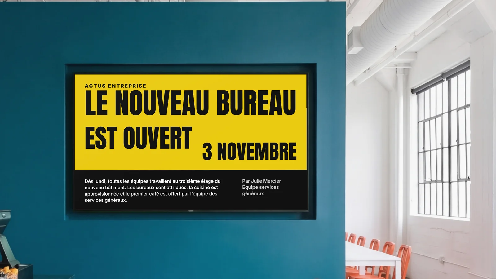 Restaurant d'entreprise avec un écran encastré dans un mur bleu canard foncé, un coin du comptoir et des chaises orange sur les côtés. L'écran affiche Actus entreprise : le nouveau bureau est ouvert, 3 novembre.