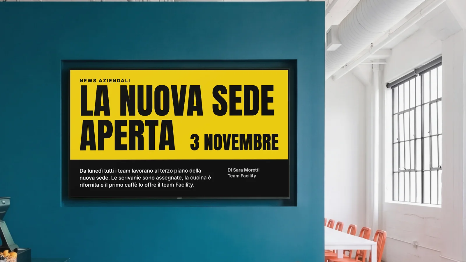 Mensa aziendale con uno schermo incassato in una parete verde petrolio scuro, un angolo del bancone e sedie arancioni ai lati. Lo schermo mostra News aziendali: la nuova sede è aperta, 3 novembre.