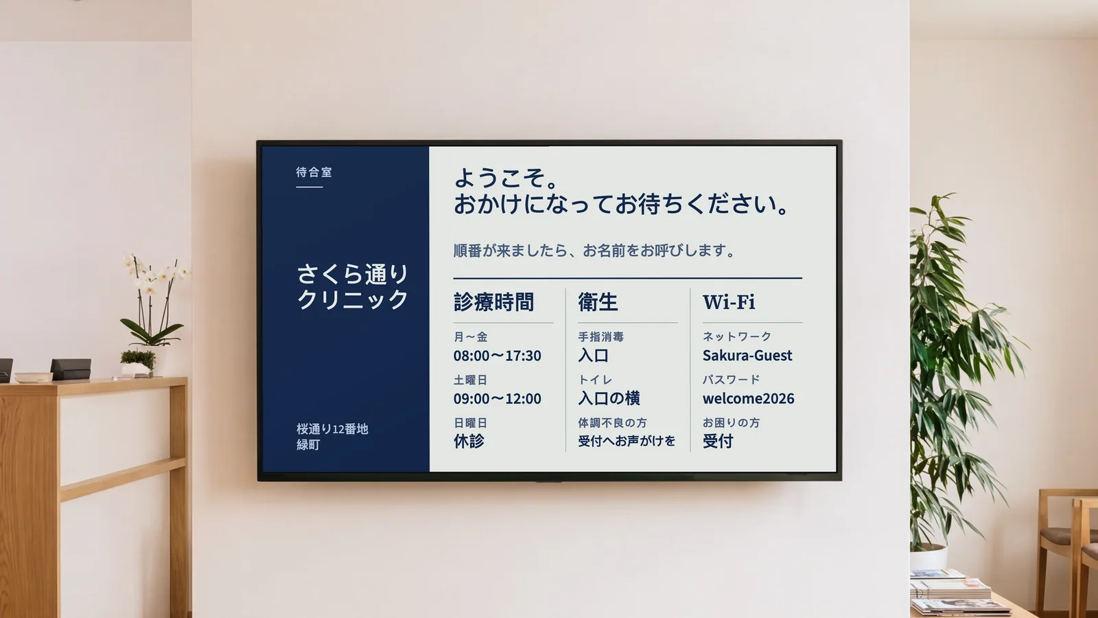 診察待ちの人が座る診療所の待合室。受付カウンターの一部とオーク材の椅子、暖かみのある白い壁の画面が見える。画面には「さくら通り クリニック」と「ようこそ。おかけになってお待ちください。」、その下に診療時間、衛生、トイレ、Wi-Fiの案内が表示されている。
