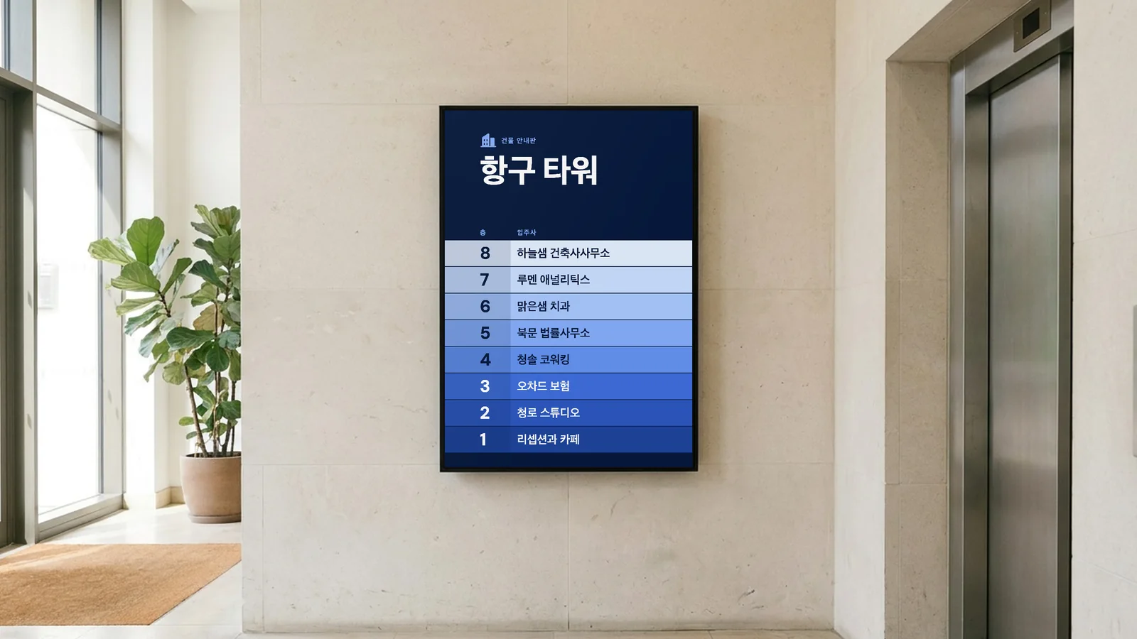 사무실 빌딩 1층 로비입니다. 밝은 석회암 벽의 철제 엘리베이터 문 옆에 세로형 화면이 있고, 왼쪽에 유리 출입구와 화분이 보입니다. 화면에 항구 타워의 건물 안내판으로 하늘샘 건축사사무소와 리셉션과 카페가 보입니다.
