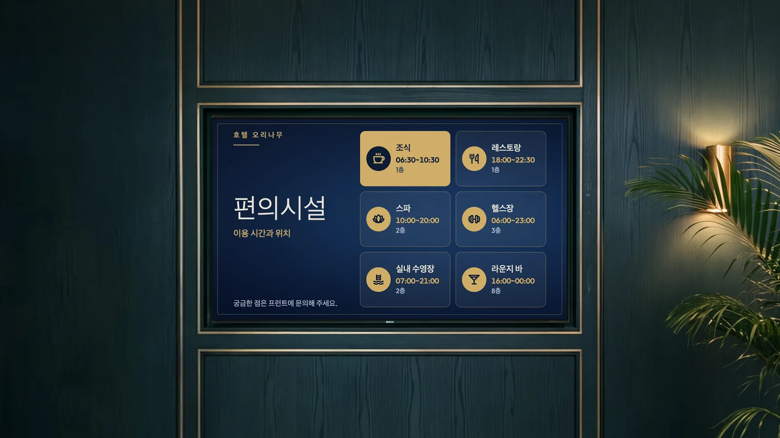 짙은 녹색 우드 패널과 황동 장식이 있는 호텔 엘리베이터 홀입니다. 화면 옆에 황동 벽등과 야자나무 화분이 있습니다. 화면에 호텔 오리나무의 편의시설인 조식, 레스토랑, 스파, 헬스장, 실내 수영장, 라운지 바가 보입니다.