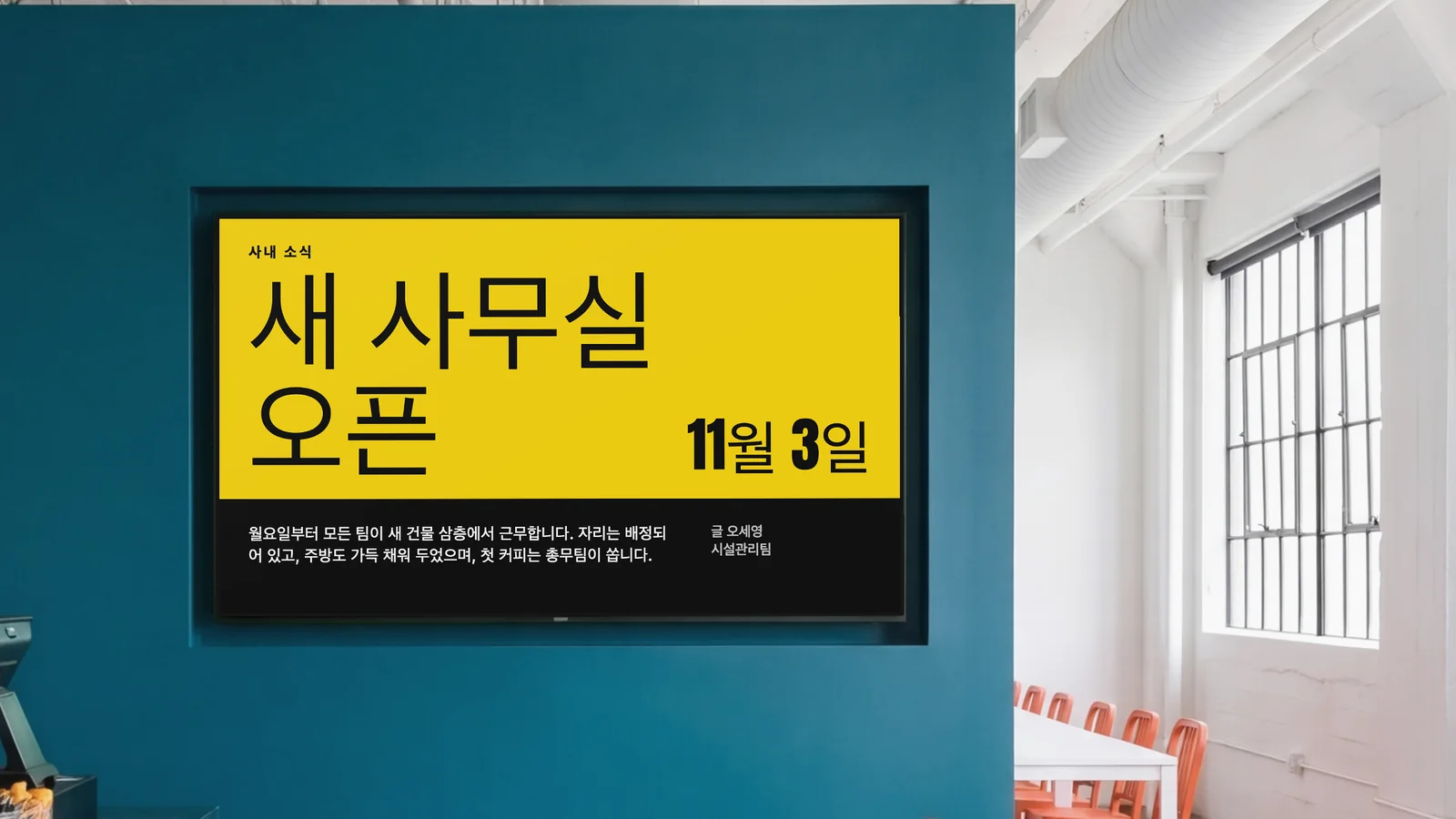 짙은 청록색 벽에 화면이 들어가 있는 직원 식당입니다. 양옆에 카운터 일부와 주황색 의자가 보입니다. 화면에는 사내 소식으로 새 사무실이 11월 3일에 오픈한다는 내용이 보입니다.