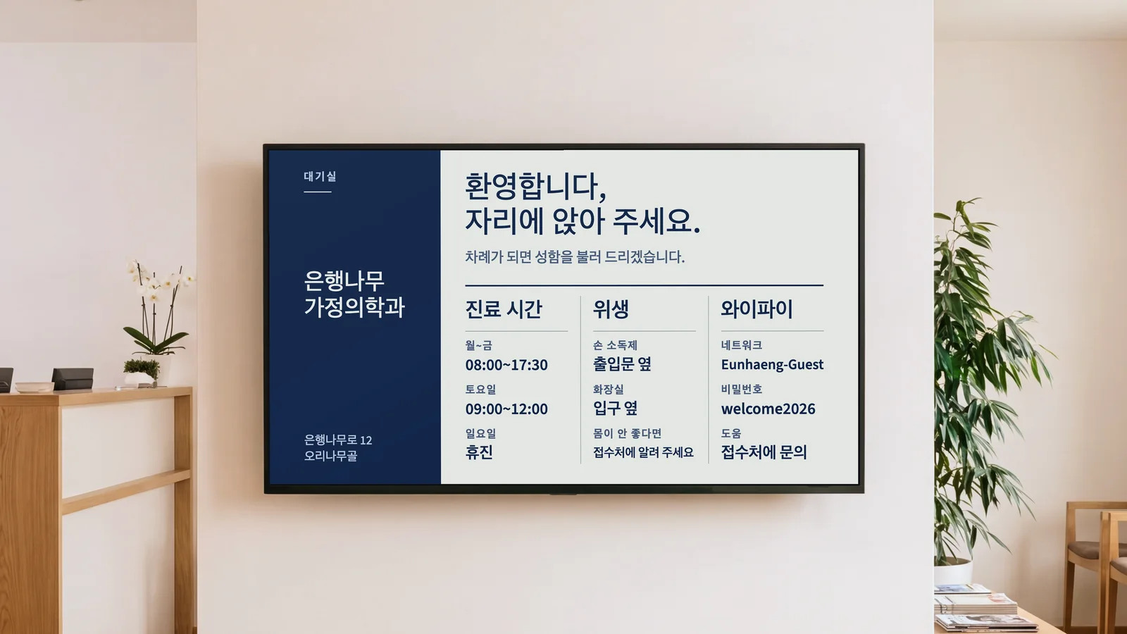 접수대 일부와 오크 대기 의자, 따뜻한 흰 벽의 화면이 보이는 가정의학과 대기실입니다. 화면에는 은행나무 가정의학과의 "환영합니다, 자리에 앉아 주세요."와 그 아래 진료 시간, 위생, 화장실, 와이파이 안내가 보입니다.