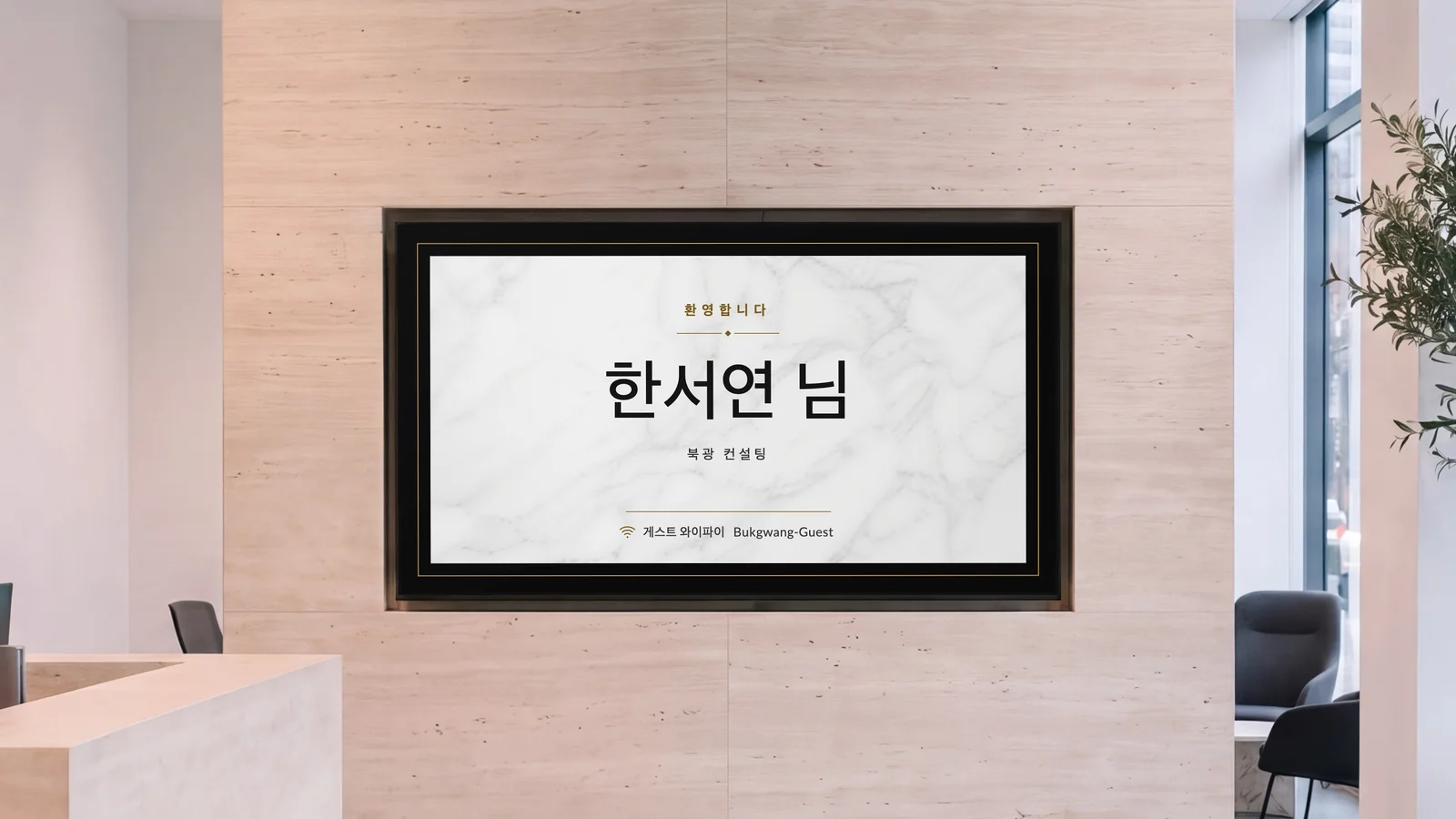 트래버틴 벽에 화면이 들어가 있는 사무실 접수 공간입니다. 양옆에 돌 접수대 모서리와 라운지 의자가 보입니다. 화면에는 "환영합니다", "한서연 님", "북광 컨설팅"이 보입니다.