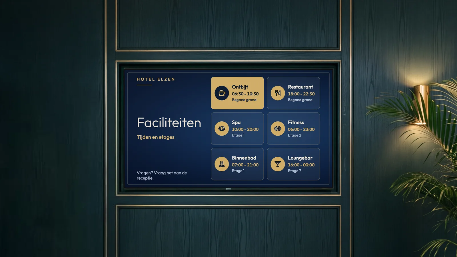 Lifthal van een stadshotel met diepgroene houten lambrisering, messing details, een messing wandlamp en een palm naast het scherm. Het scherm toont de faciliteiten van Hotel Elzen: ontbijt, restaurant, spa, fitness, binnenbad en loungebar.