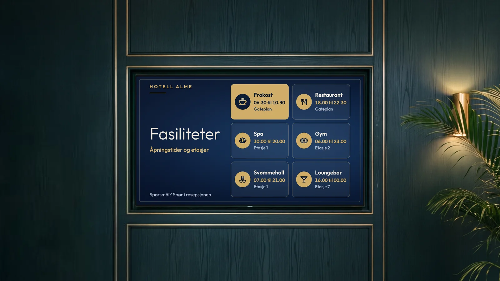 Heislobby på et byhotell med dyp grønn trepanel, messingdetaljer, en messinglampe og en palme ved siden av skjermen. Skjermen viser fasilitetene på Hotell Alme: frokost, restaurant, spa, gym, svømmehall og loungebar.